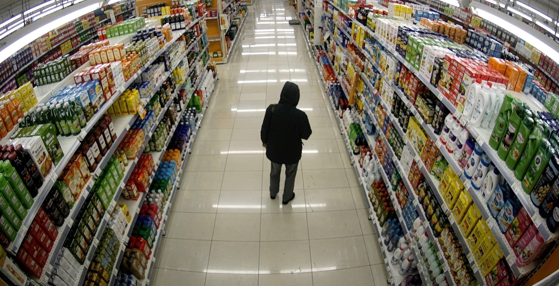Ceiling camera view of a supermarket aisle, a hooded figure at the shelves
